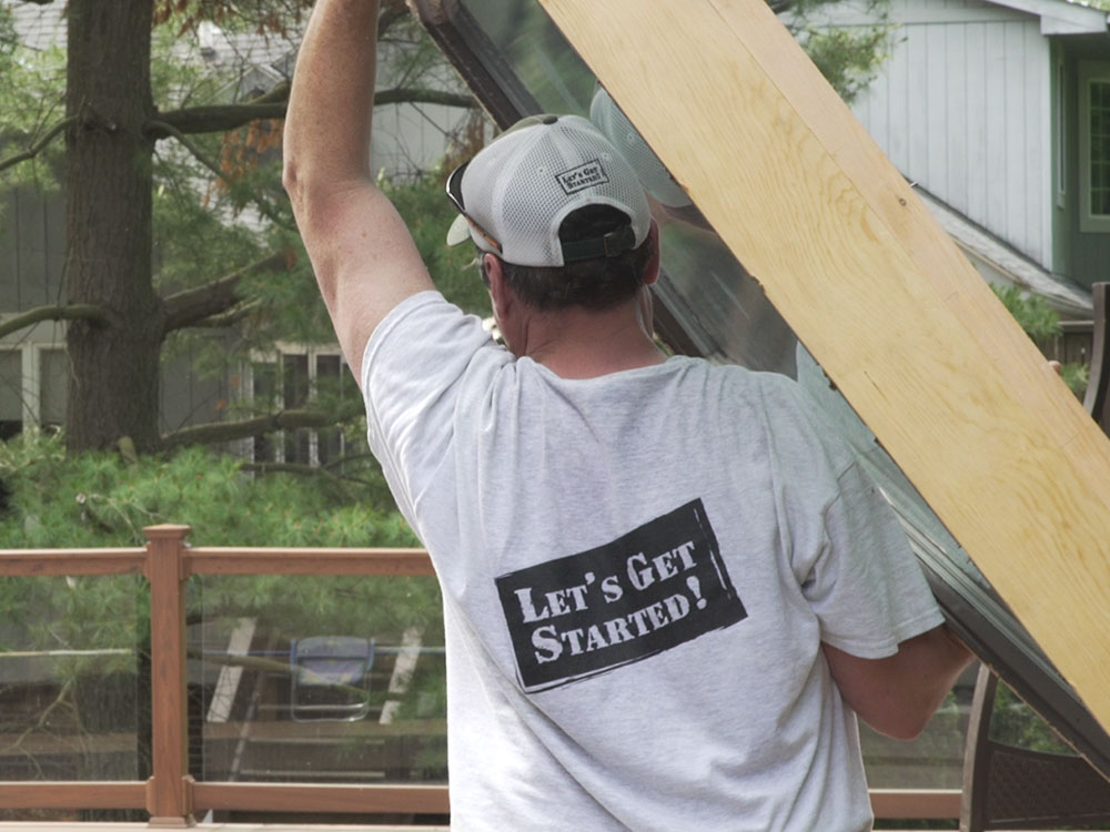 Man wearing t-shirt with Let's Get Started logo on the back; he's carrying a window